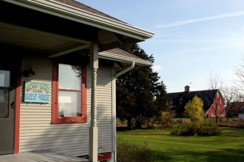 A cozy guest house with a sign, surrounded by green grass and trees, with a red barn in the background under a clear sky.