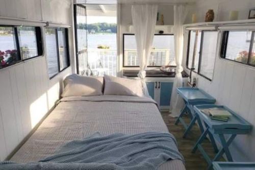 Cozy interior of a small, bright living space with a bed, blue accents, and large windows overlooking a lake.