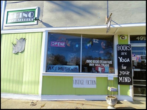 A storefront with a green exterior, featuring signs for books, art, and music, and a "Vintage Fiction" banner.