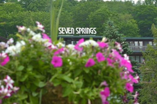 A vibrant flower arrangement in the foreground with the "Seven Springs" sign and green trees in the background.