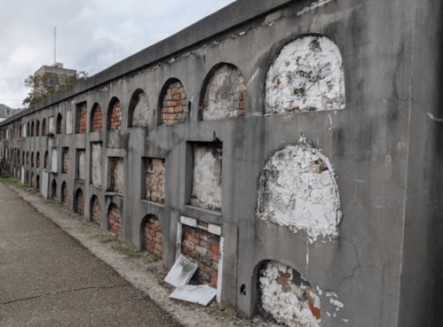 A weathered wall with arched openings, showing exposed bricks and peeling paint, along a pathway.