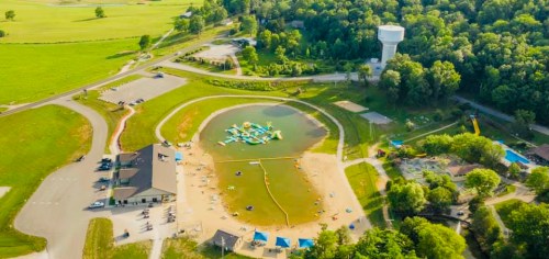 Aerial view of a recreational area with a sandy beach, water activities, and a water tower surrounded by greenery.