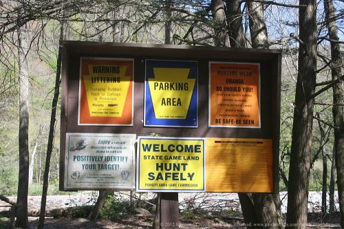 A signboard with various warnings and guidelines about littering, parking, and safe hunting practices in a wooded area.