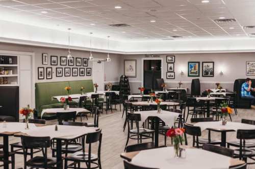 A spacious restaurant with tables set for dining, adorned with flowers and framed photos on the walls.