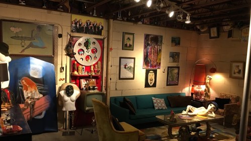 A cozy, eclectic room featuring colorful artwork, a green couch, and unique decor items on the walls and furniture.