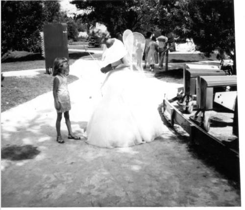 A young girl interacts with a woman in a fairy costume in a park setting.