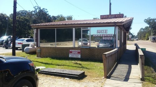 A small, brick building with large windows, featuring a sign that reads "Mize Hamburger House" and a wooden walkway.