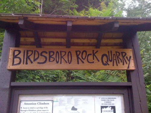 Sign for Birdsboro Rock Quarry, featuring bold lettering and surrounded by greenery. Climbing information is posted below.