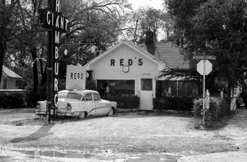 A vintage diner named "Red's" with a classic car parked outside, surrounded by trees and a street sign.