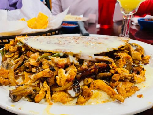 A large plate of sizzling chicken fajitas topped with melted cheese, served with chips in a restaurant setting.