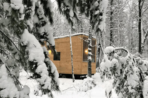 A cozy wooden cabin nestled in a snowy forest, surrounded by snow-covered trees. Warm lights glow from the windows.