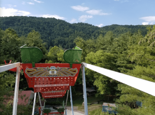 View from the top of a Ferris wheel overlooking green mountains and trees under a clear blue sky.