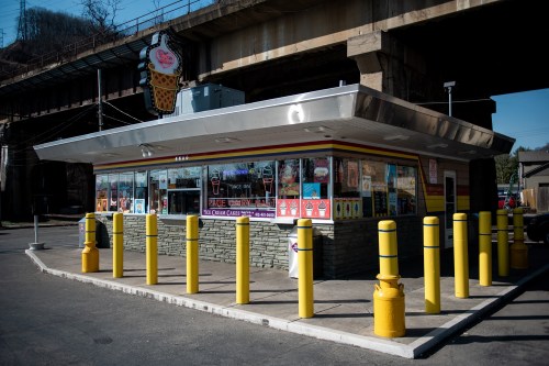 A colorful ice cream shop with yellow safety poles, located under a bridge on a sunny day.