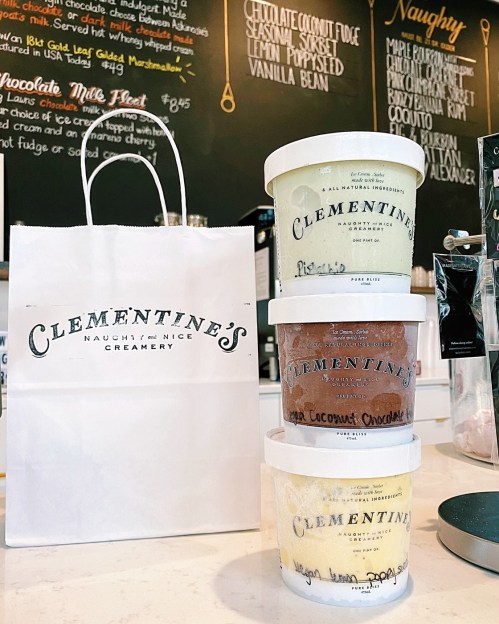 Three ice cream tubs stacked next to a Clementine's Creamery bag, with a menu board in the background.