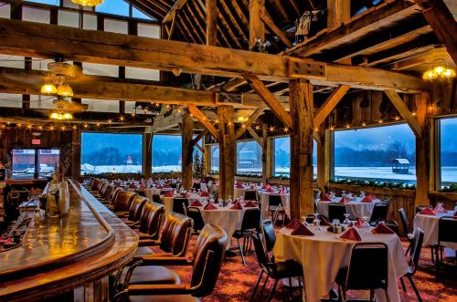 Cozy restaurant interior with wooden beams, round tables set for dining, and large windows overlooking a snowy landscape.
