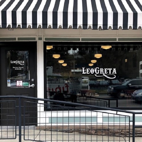 Exterior of a restaurant named "LeoGreta," featuring a striped awning and large glass windows.