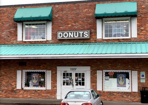 A brick storefront with a teal awning and a sign reading "DONUTS," featuring large windows and a parked car in front.