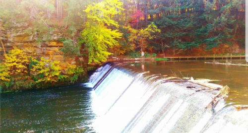 A serene waterfall cascading over a rocky ledge, surrounded by vibrant autumn foliage and calm waters.