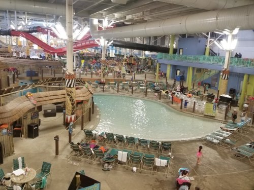 A large indoor water park featuring a pool, slides, and various seating areas, with many people enjoying the space.