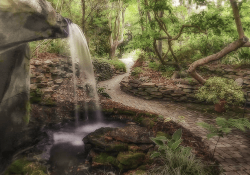 A serene garden scene featuring a waterfall, stone path, and lush greenery.