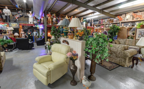 A spacious store filled with furniture, decor, and mannequins, featuring a light-colored recliner and plants.