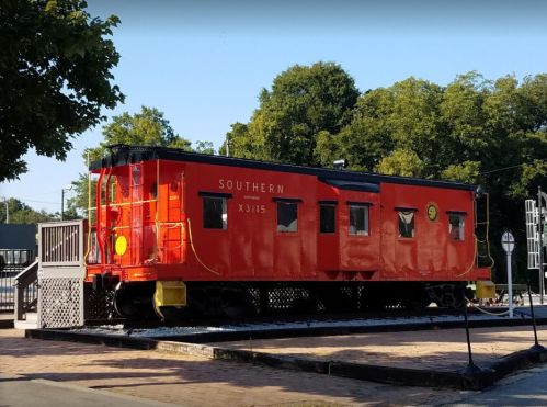 A bright red train caboose labeled "Southern" parked on a platform surrounded by trees.