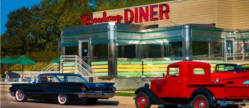 A classic diner with a retro design, featuring vintage cars parked outside in bright colors.