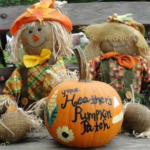 Two scarecrows sit beside a painted pumpkin that reads "Heather's Pumpkin Patch," surrounded by small decorative gourds.