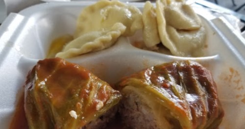 A takeout container with stuffed cabbage rolls and dumplings in a savory sauce.