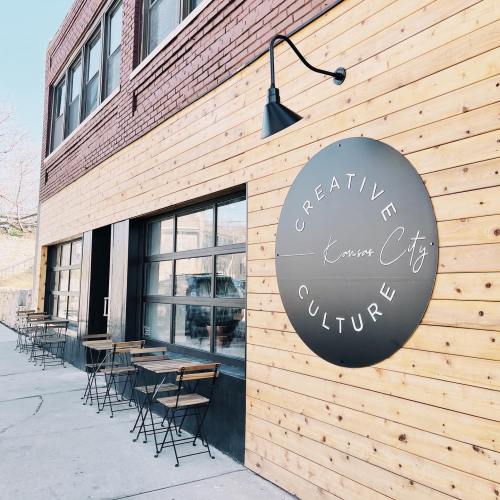 Exterior of a building with a wooden facade and a sign reading "Creative Culture Kansas City," featuring outdoor seating.