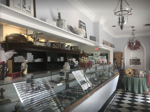 A charming chocolate shop interior with a glass display case filled with various chocolates and a checkered floor.