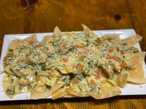 A plate of nachos topped with creamy cheese, spinach, diced tomatoes, and herbs on a wooden table.