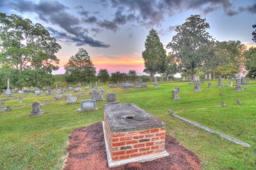 A serene cemetery at sunset, featuring gravestones and lush green grass under a colorful sky.