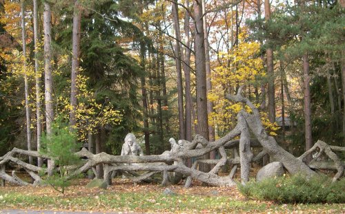 A whimsical stone sculpture of animals among trees, surrounded by autumn foliage in a serene forest setting.