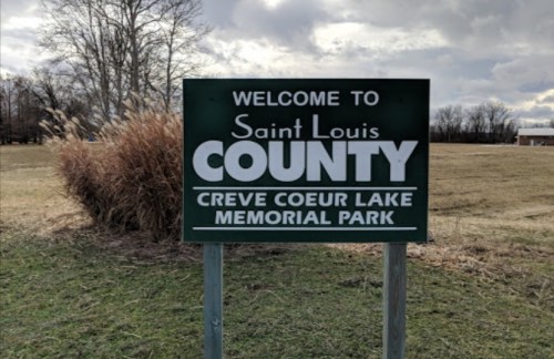 Welcome sign for Saint Louis County, Creve Coeur Lake Memorial Park, with grassy area and cloudy sky in the background.