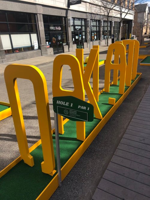 A colorful mini-golf setup with a sign for Hole 1, labeled "PAR 1," in an urban area.