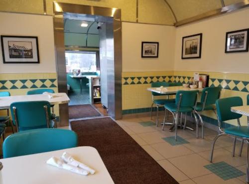 A retro diner interior with teal chairs, white tables, and framed photos on the walls, leading to an entrance.
