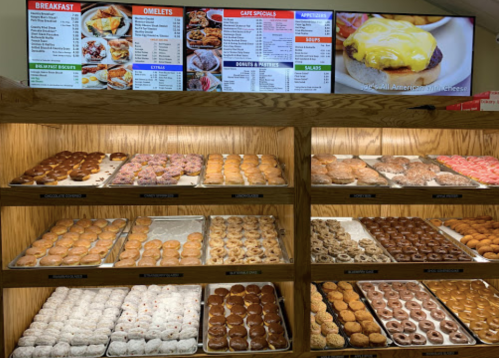 A display case filled with various donuts and pastries, with a menu board above listing breakfast and cafe specials.