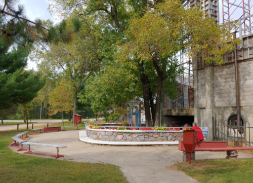 A landscaped park area with benches, a stone wall, and trees, next to a building under construction.