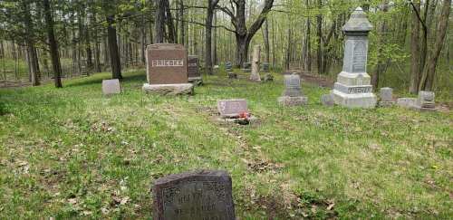 A serene cemetery scene with several gravestones surrounded by trees and greenery.