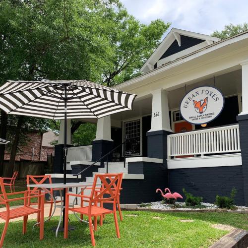 A charming outdoor seating area with orange chairs and a striped umbrella in front of a cozy bakery.