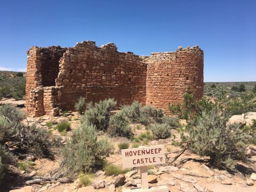 Ruins of Hovenweep Castle, a stone structure surrounded by desert vegetation under a clear blue sky.