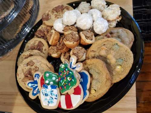 A black platter filled with various cookies, including decorated holiday cookies, chocolate chip, and coconut macaroons.