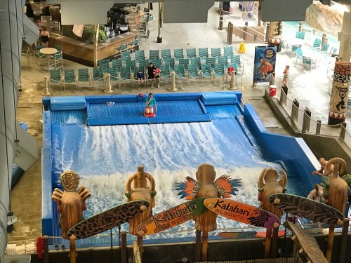 A water park scene featuring a wave pool with people surfing and colorful decor around the area.