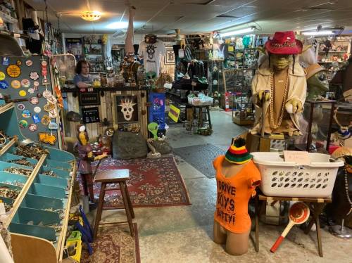 A cluttered antique shop filled with eclectic items, including clothing, decor, and a mannequin wearing an orange shirt.