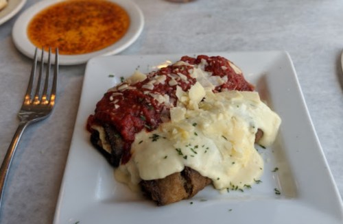 A plate of enchiladas topped with red and white sauces, garnished with cheese and herbs, served with a side of sauce.