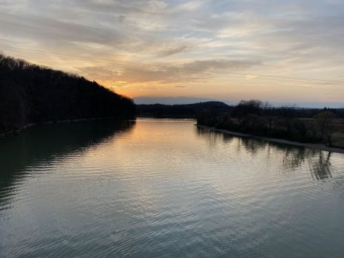 A serene river at sunset, reflecting the colorful sky and surrounded by trees and hills.