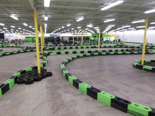 A go-kart track with black and green barriers, featuring winding curves and a spacious indoor setting.