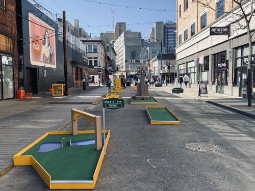A vibrant street scene featuring a mini-golf course with colorful holes and obstacles in an urban setting.