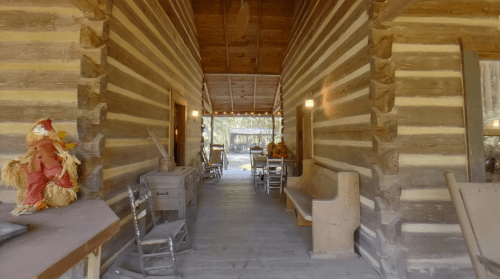 A rustic log cabin interior with wooden walls, a long hallway, and a scarecrow decoration at the entrance.